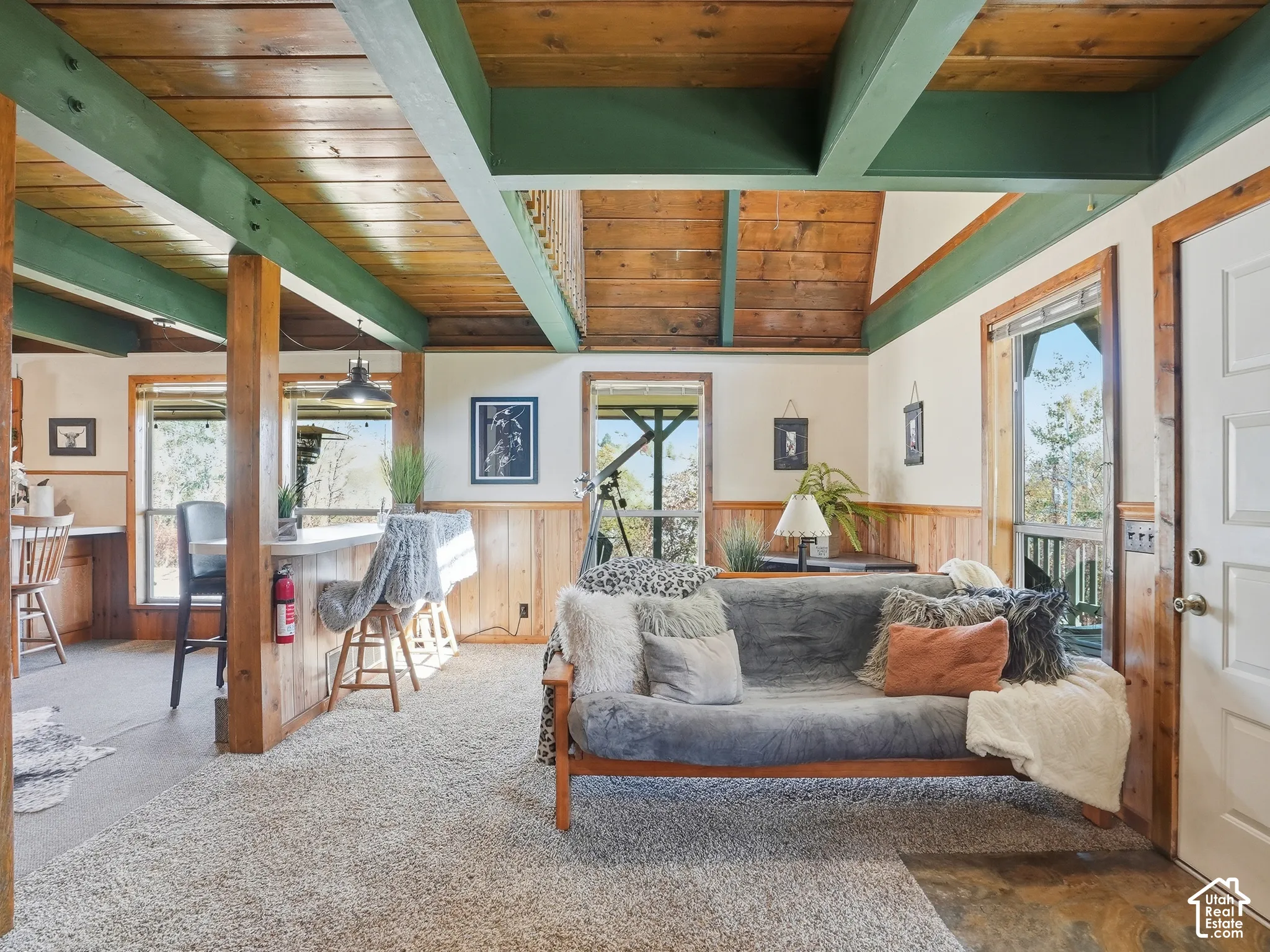 Exposed timber ceiling beams, natural wood-plank ceiling, wood wainscoting, multiple windows, and a raised breakfast bar