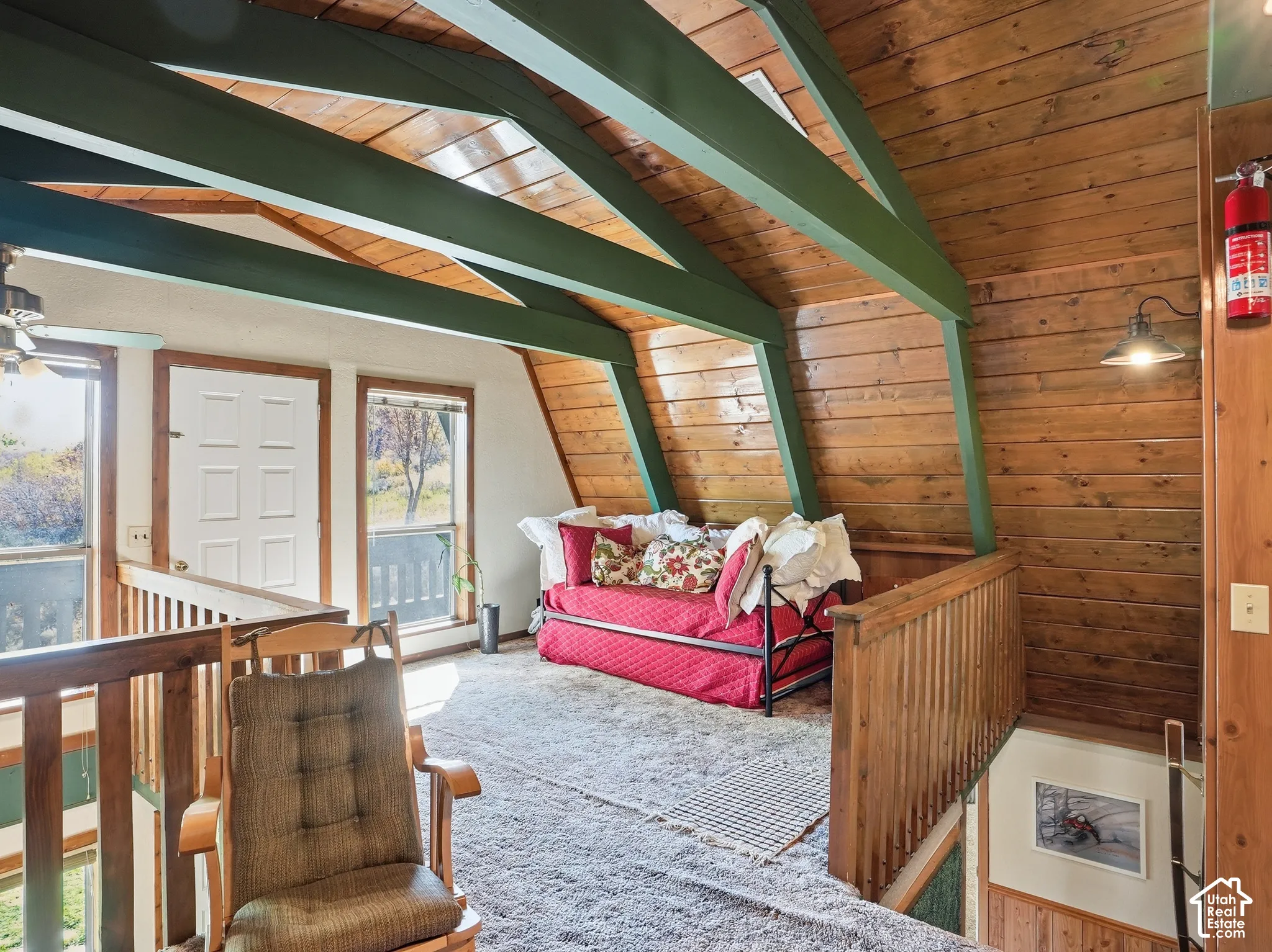 Vaulted ceiling featuring exposed structural beams, wood-paneled walls, carpeted flooring, and a wood railing