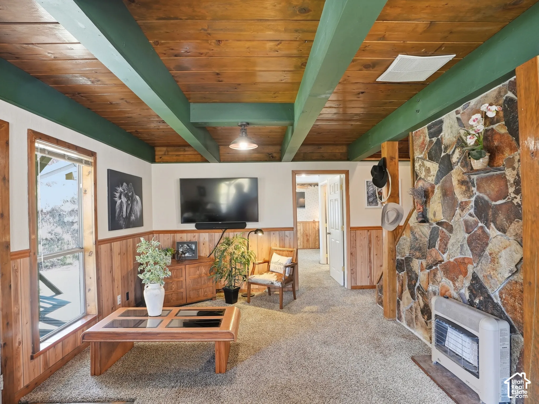 Exposed wood-plank ceiling with painted beams, stone-clad fireplace feature wall, wood-paneled wainscoting, and large picture window