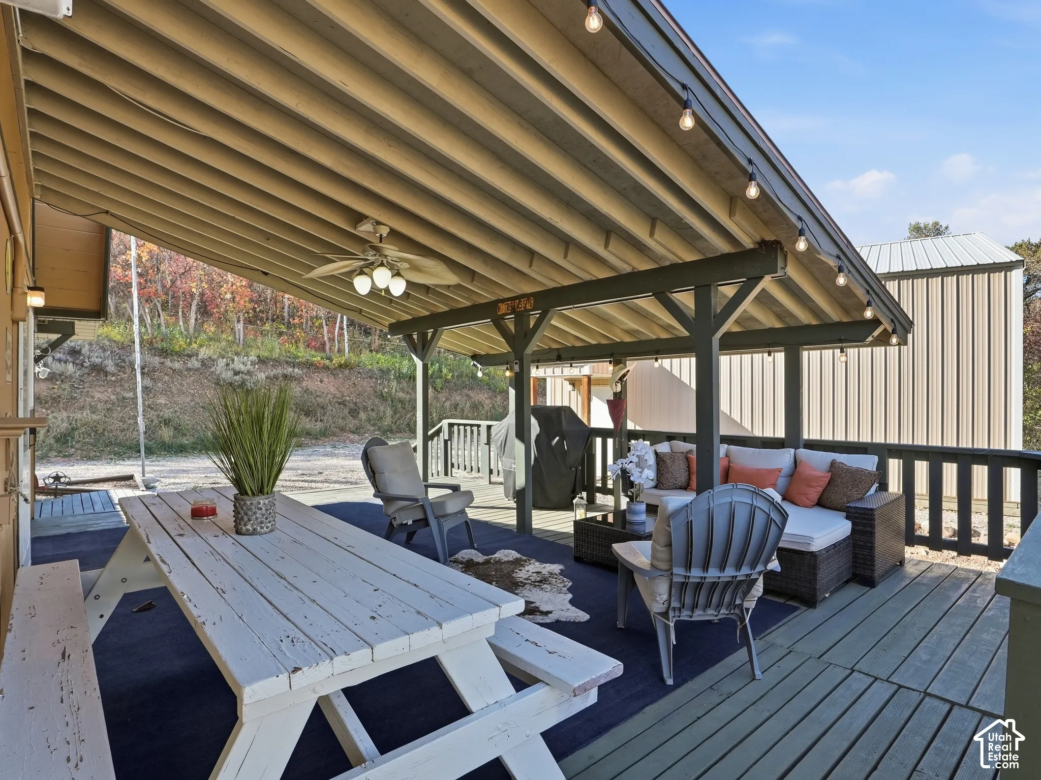 Covered deck featuring exposed beam ceiling, integrated string lighting, and a ceiling-mounted fan