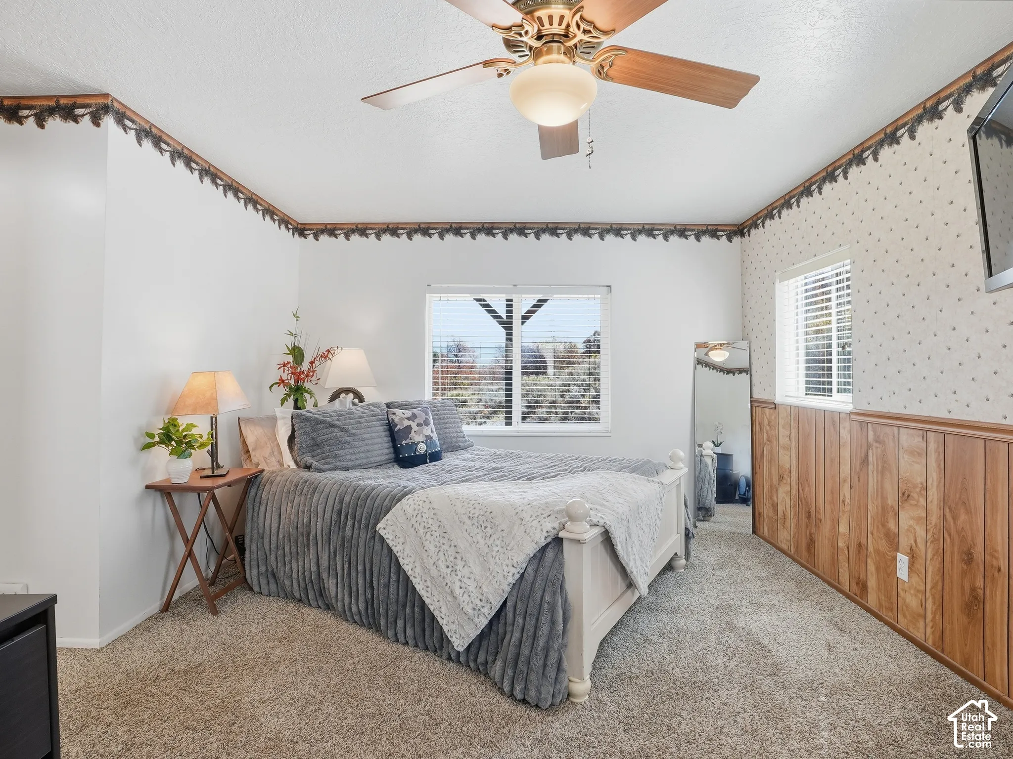 Room featuring carpeted flooring, wood-finish wainscoting, a ceiling fan with integrated lighting, and dual windows