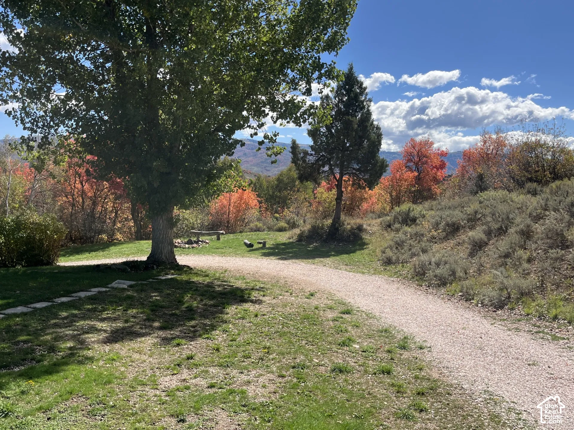 Expansive outdoor space featuring a gravel pathway, mature trees, natural landscaping, and distant mountains