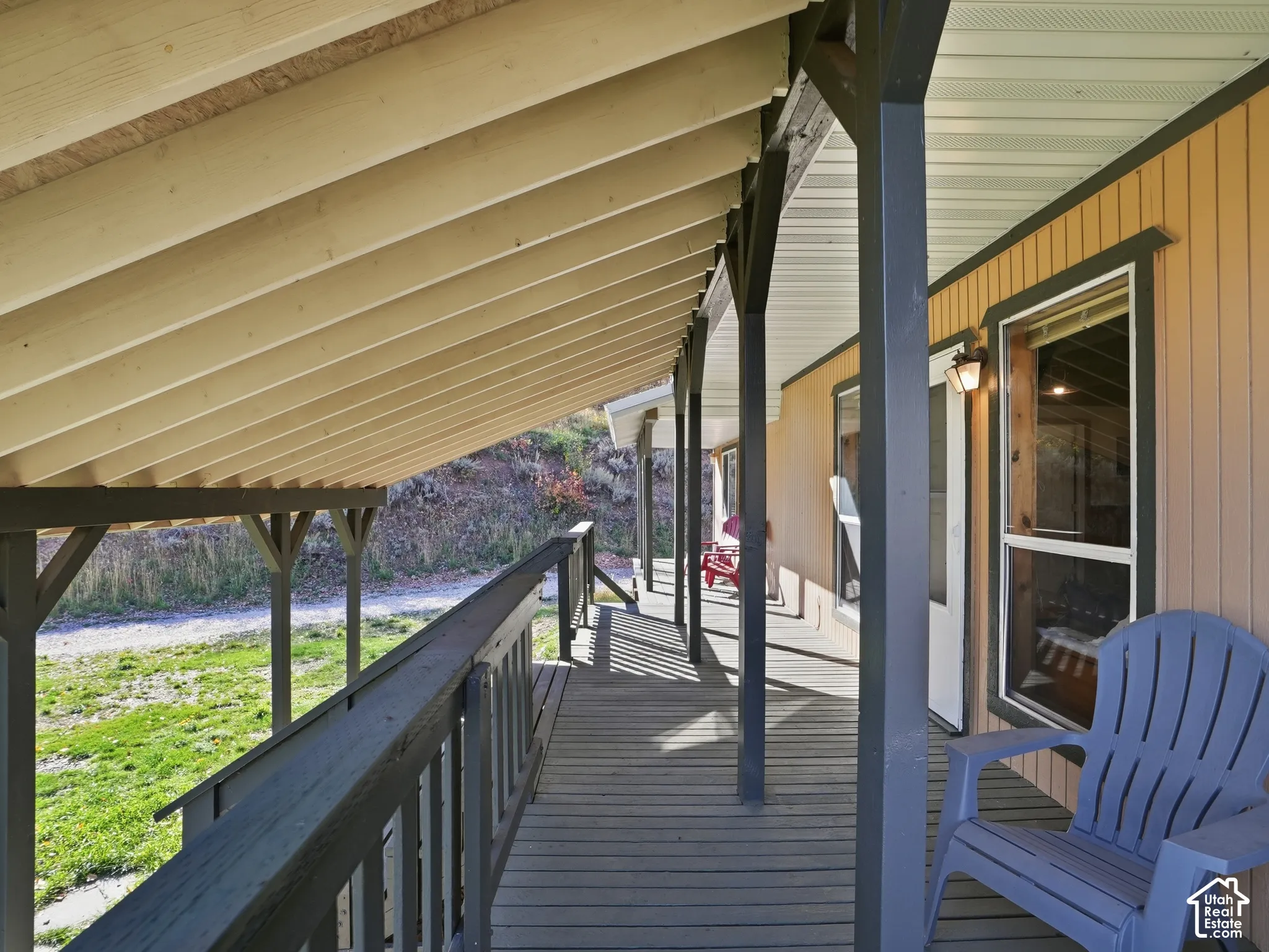 Covered wooden deck featuring an exposed rafter ceiling, vertical siding, and a wooden railing