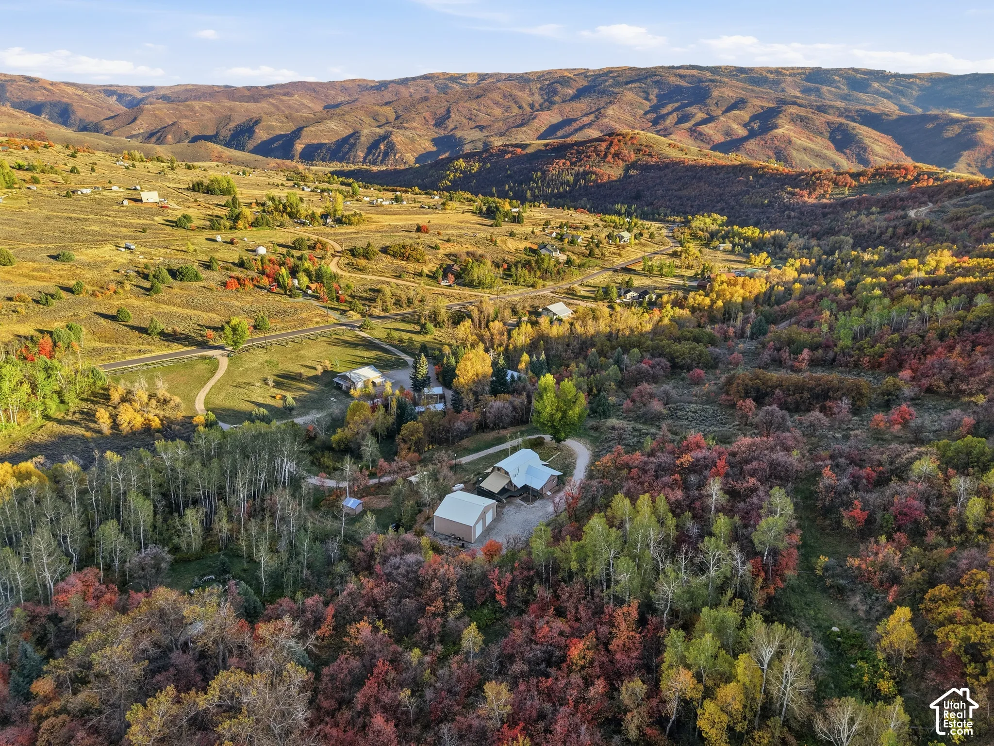 Aerial perspective of mountain acreage featuring a metal-roofed residence, detached garage, and extensive wooded terrain