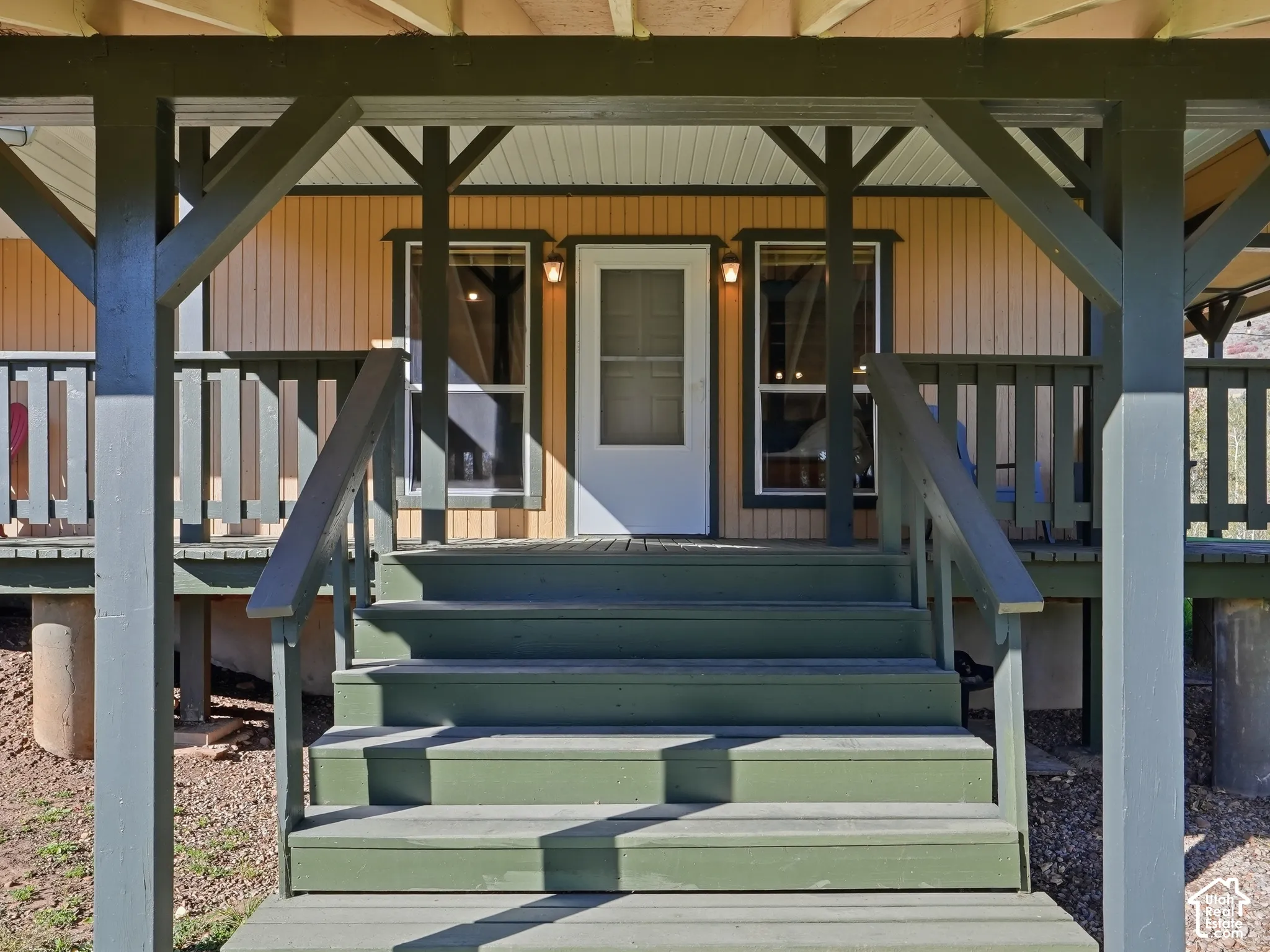 Covered wooden front porch with stairs, vertical siding, and exterior wall-mounted light fixtures