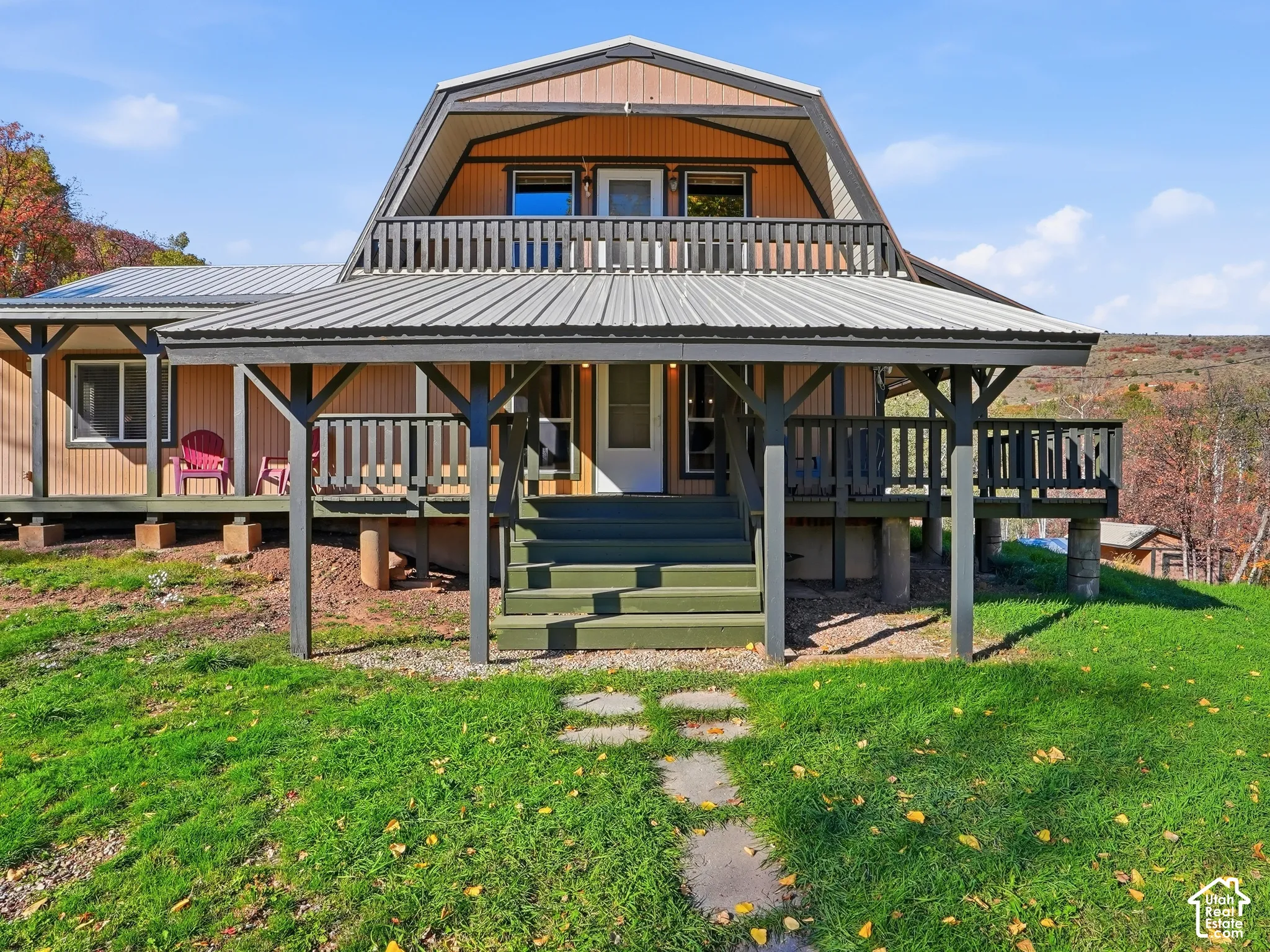 Gambrel-roof exterior featuring a covered wraparound porch, upper-level balcony with railing, metal roofing, and vertical siding