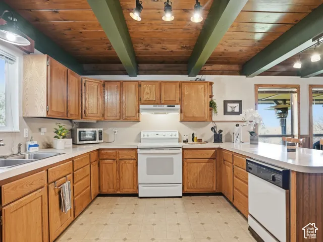 Kitchen featuring wood-finished cabinetry, exposed wood ceiling beams, laminate countertops, and white appliances