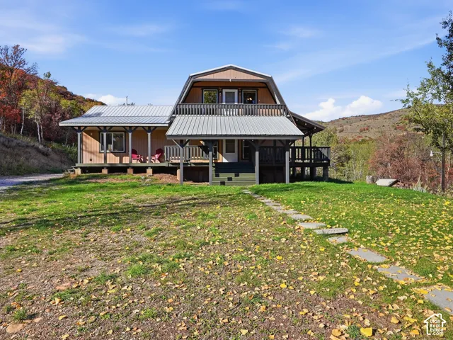Gambrel-style exterior featuring a metal roof, tiered wrap-around deck, upper-level balcony, and stone paver walkway