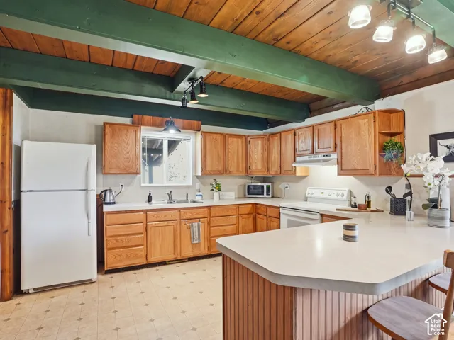Kitchen featuring wood-paneled ceiling with exposed beams, wood cabinetry, solid surface countertops, and adjustable track lighting