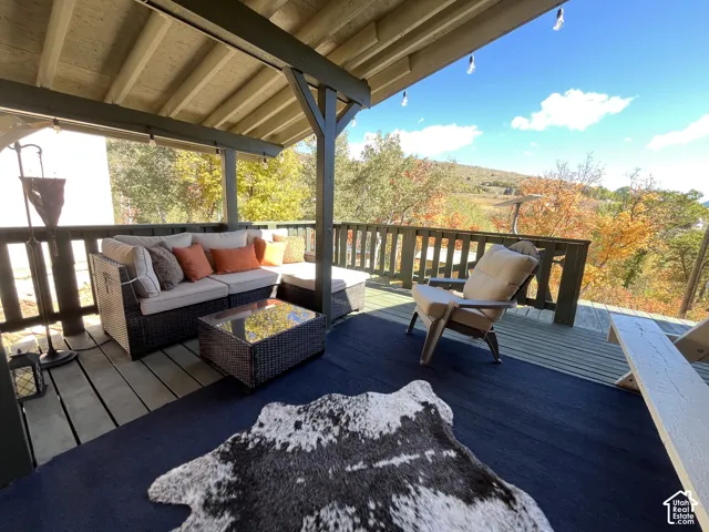 Covered outdoor deck with exposed wood beam ceiling, string lighting, and wood railing