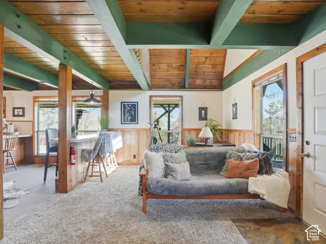Exposed timber ceiling beams, natural wood-plank ceiling, wood wainscoting, multiple windows, and a raised breakfast bar