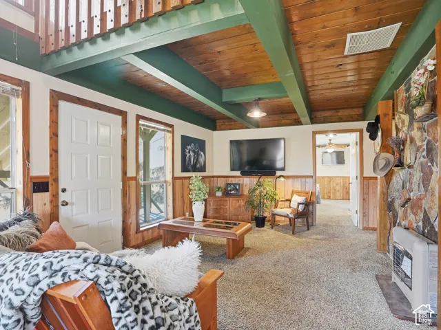 Exposed wood-beam ceiling, natural stone fireplace surround, wood paneling, and interior balcony featuring a wooden railing