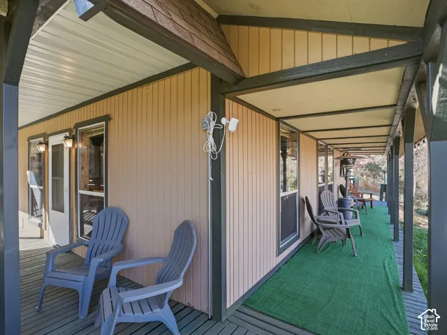 Covered exterior porch featuring vertical siding, dark wood-finish support beams, and wall-mounted exterior lighting fixtures