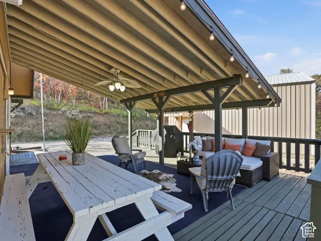Covered deck featuring exposed beam ceiling, integrated string lighting, and a ceiling-mounted fan