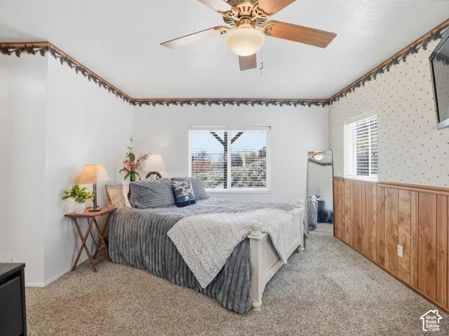 Room featuring carpeted flooring, wood-finish wainscoting, a ceiling fan with integrated lighting, and dual windows