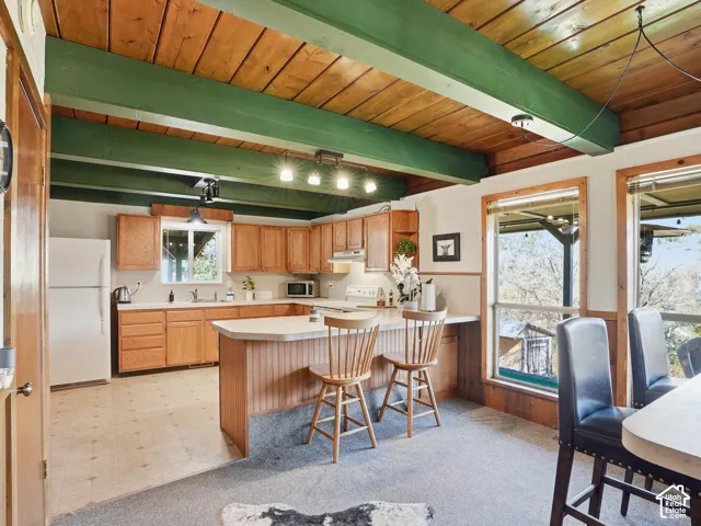 Kitchen featuring wood cabinetry, solid-surface countertops, wood-plank ceiling, and exposed painted beams