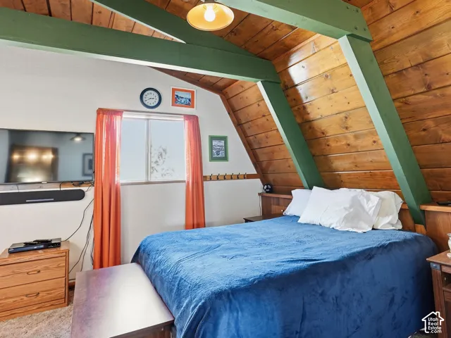 Vaulted ceiling featuring exposed structural beams, natural wood-paneled walls, and a built-in wooden headboard