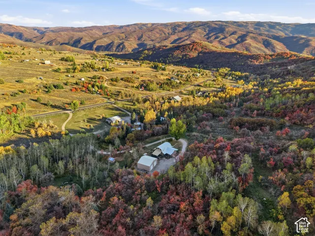 Aerial perspective of mountain acreage featuring a metal-roofed residence, detached garage, and extensive wooded terrain