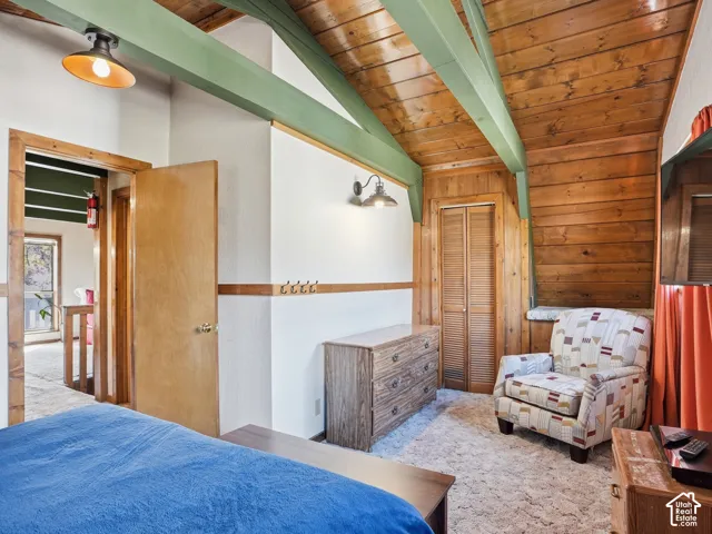 Vaulted ceiling with exposed wood-finish beams, wood-plank ceiling treatment, and built-in louvered closet doors