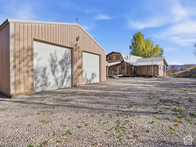 Detached metal-sided garage with two roll-up doors, gravel drive, and multi-story residence with a metal roof