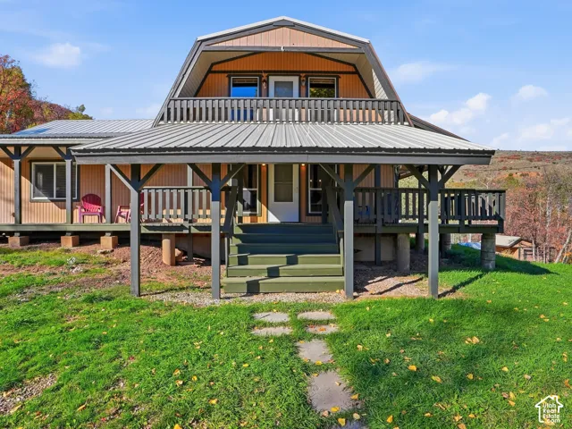 Gambrel-roof exterior featuring a covered wraparound porch, upper-level balcony with railing, metal roofing, and vertical siding