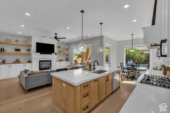 Open-concept living space with wood-finish flooring, a kitchen island with stone countertops, a gas range, and a fireplace with built-in cabinetry and shelving