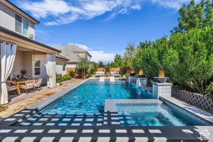 Expansive outdoor living area featuring a rectangular swimming pool, integrated spa, covered patio with flagstone flooring, and multiple fire bowls with decorative tile bases