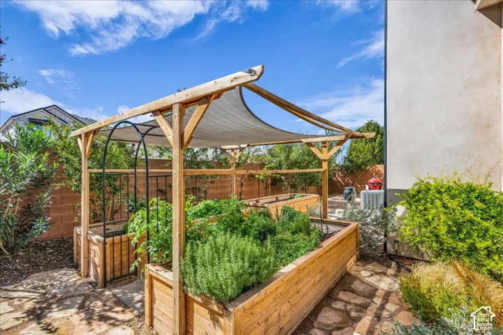 Outdoor garden area featuring multiple raised wooden planter boxes, a wooden pergola with a shade cover, and flagstone pathways