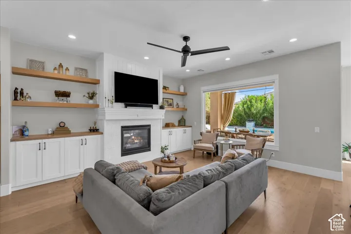 Open-concept living room featuring a gray upholstered sectional sofa, wood-finish flooring throughout, and abundant natural light from sliding glass doors opening to an outdoor patio