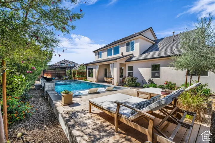 Expansive backyard featuring a built-in swimming pool, wood-finish decking, lush landscaping, and a stucco exterior