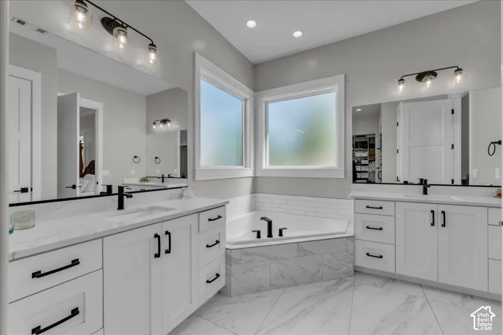 Dual white vanities with black hardware, an inset bathtub with subway tile surround, white countertops, and a large wall mirror