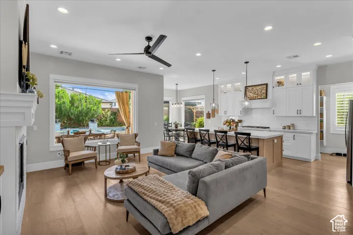 Open-concept living area featuring wood-finish flooring, a white fireplace with a mantel, and recessed lighting