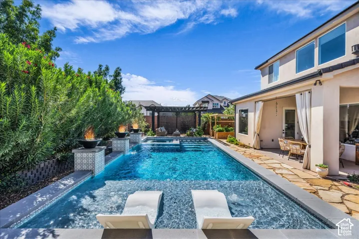 Sparkling swimming pool with integrated tanning ledge, natural stone patio, and stucco exterior with multiple windows