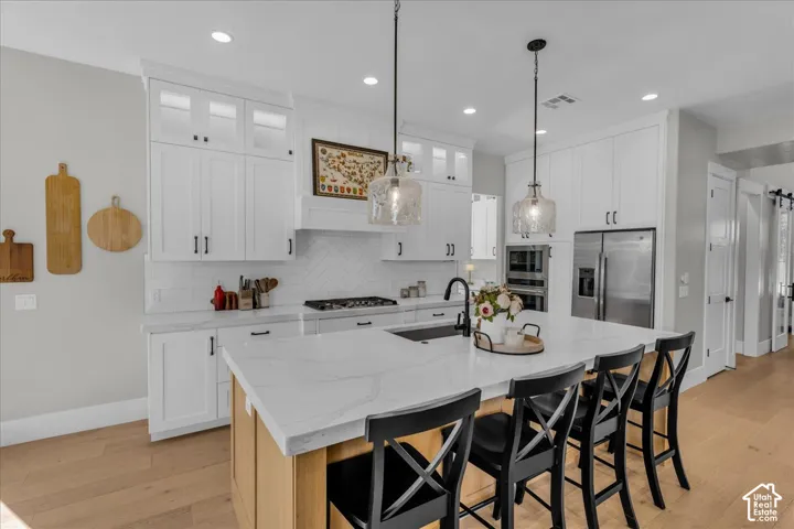 Expansive kitchen island with seating, white shaker-style cabinetry, stainless steel appliances, herringbone tile backsplash, and light wood-finish flooring
