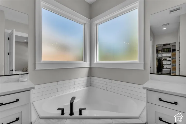 Corner soaking tub with matte black fixtures, subway tile surround, two windows, and dual vanity areas with white cabinetry and dark hardware