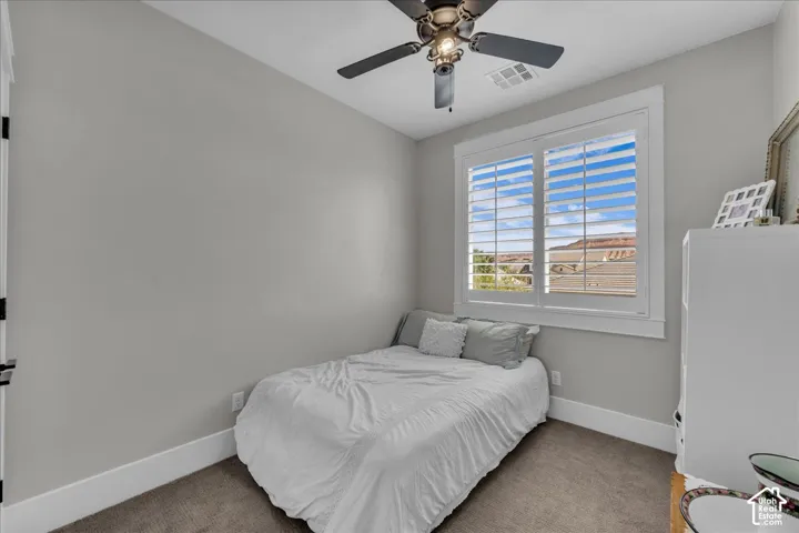 Recessed window with white plantation shutters, neutral gray wall paint, dark carpet flooring, and a ceiling fan with light fixture