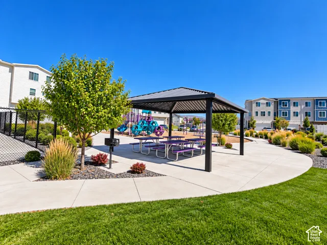 Paved patio with a slatted pergola, surrounded by landscaped greenery and a grass lawn