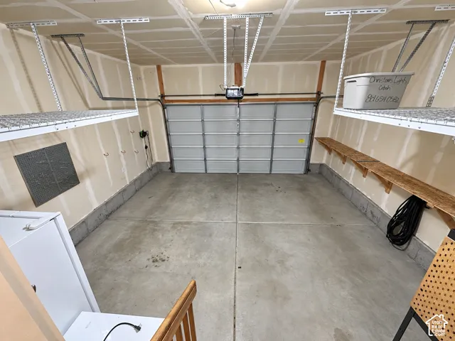 Attached garage featuring a sectional overhead door, concrete flooring, overhead wire shelving, and built-in wood shelving