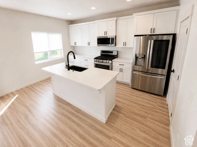 Kitchen featuring white shaker cabinetry, stainless steel appliances, a center island with a black sink and faucet, white countertops, and wood-finish flooring