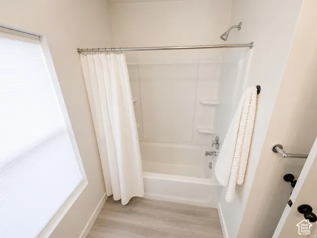 Bathtub with an integrated shower, chrome fixtures, and light wood-finish flooring