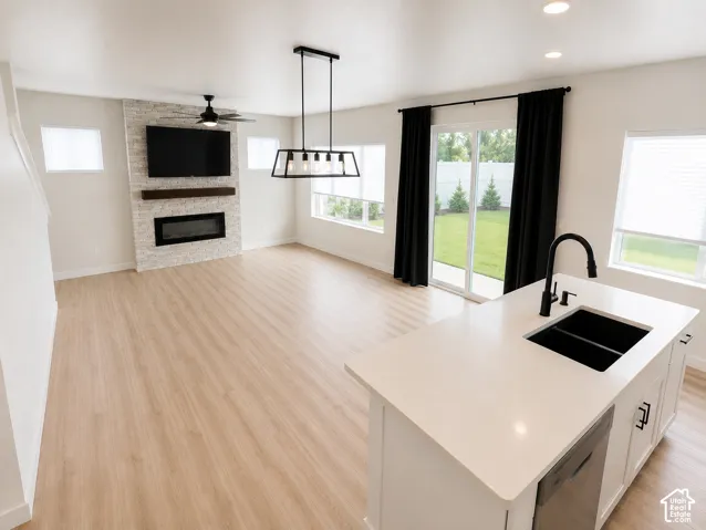 Open-concept living area with wood-finish flooring, a stone-accented fireplace, and a ceiling fan