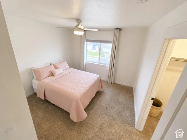 Recessed window with drapes, ceiling fan with integrated lighting, carpeted flooring, and a closet with a hanging rod
