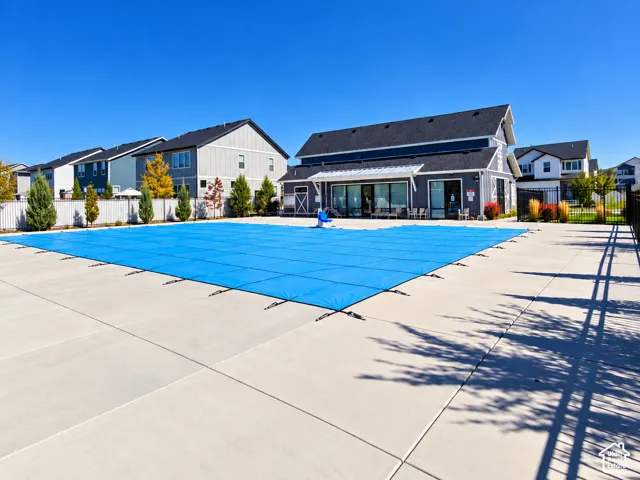 Community pool with expansive concrete decking, a modern clubhouse, and a surrounding security fence
