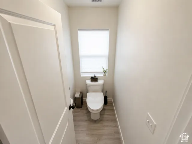 Powder room with a modern toilet, integrated window blind, and wood-finish flooring