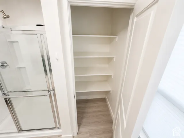 Built-in shelving, glass-enclosed shower with chrome fixtures, wood-finish flooring