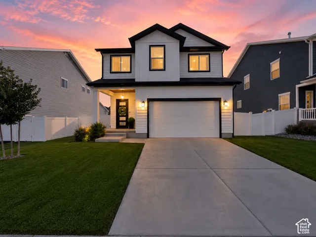 Contemporary two-story exterior with white siding and black trim, featuring a concrete driveway, attached garage, covered entry, and a manicured lawn