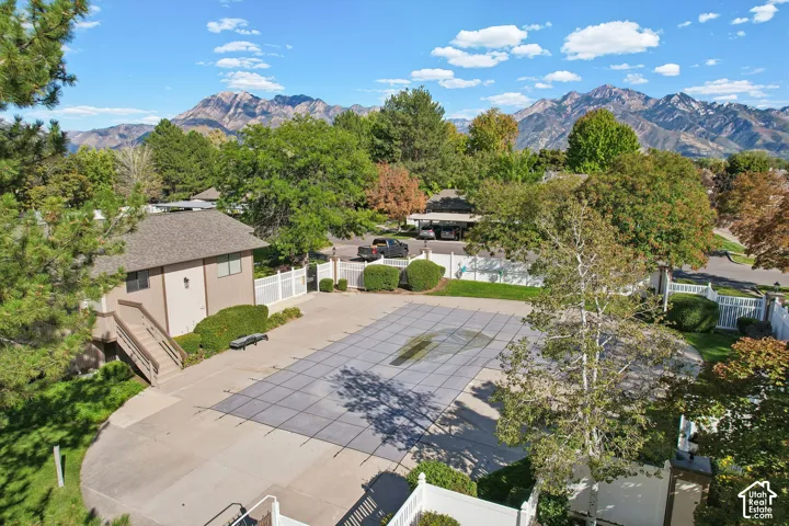 Community pool with protective cover, adjacent building with exterior stairs, white fencing, and mature landscaping
