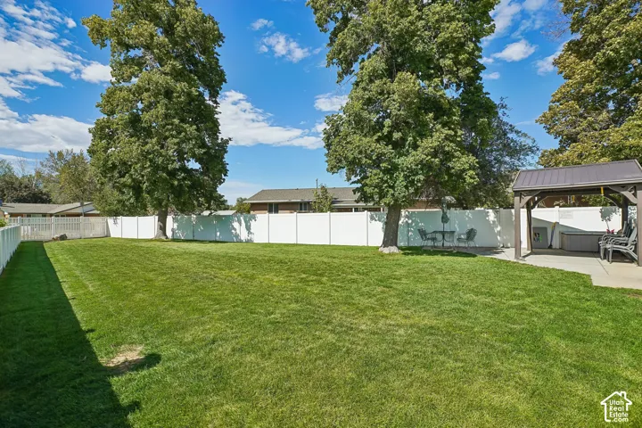 Expansive green lawn with mature shade trees, bordered by a white privacy fence