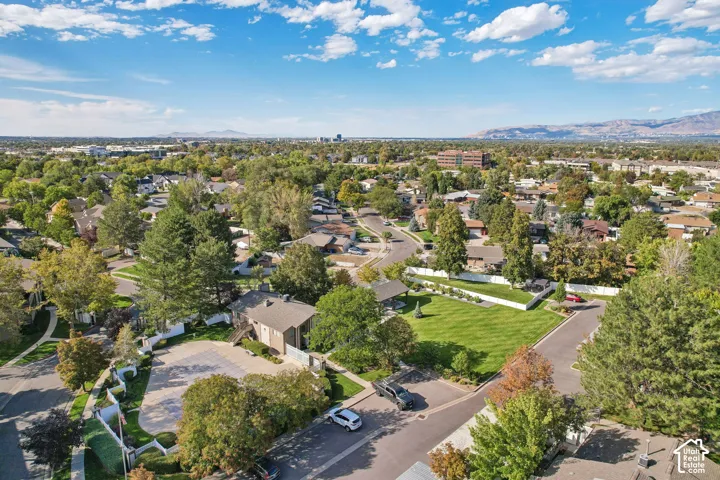 Aerial perspective showcasing a manicured lawn with mature landscaping, circular driveway with paved hardscaping, and a residential setting nestled within an established tree-lined neighborhood with distant mountain backdrop