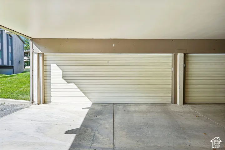 Concrete parking area with a corrugated metal garage door and a beige exterior wall